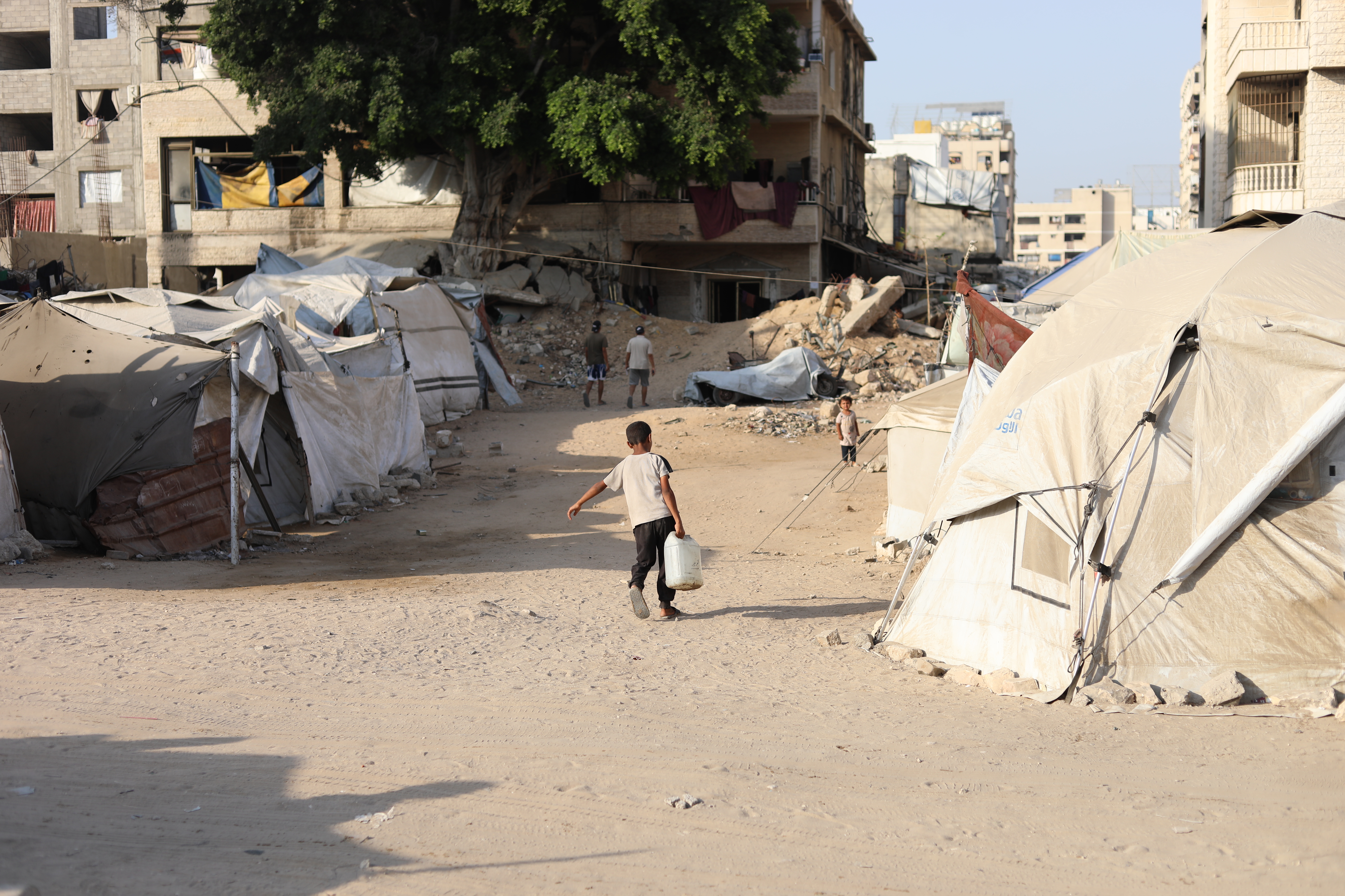 Un petit garçon lutte sous le poids d'un jerrycan d'eau pour le ramener à la tente de sa famille déplacée.